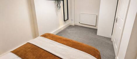 Un dormitorio con cama, radiador, armario y estante de pared con una planta.