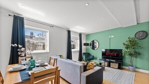 A modern living room with a dining area, a sofa, a TV, and a potted plant. - Spacious Bristol Apartment - Parking & WIFI (Bristol)