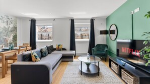 A modern living room with a sectional sofa, a glass coffee table, a flat-screen TV, and a view of the outside. - Spacious Bristol Apartment - Parking & WIFI (Bristol)