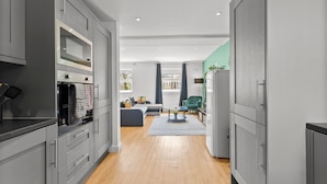 A modern kitchen with grey cabinets, a built-in oven, and a dining area with a grey sofa and a small table. - Spacious Bristol Apartment - Parking & WIFI (Bristol)