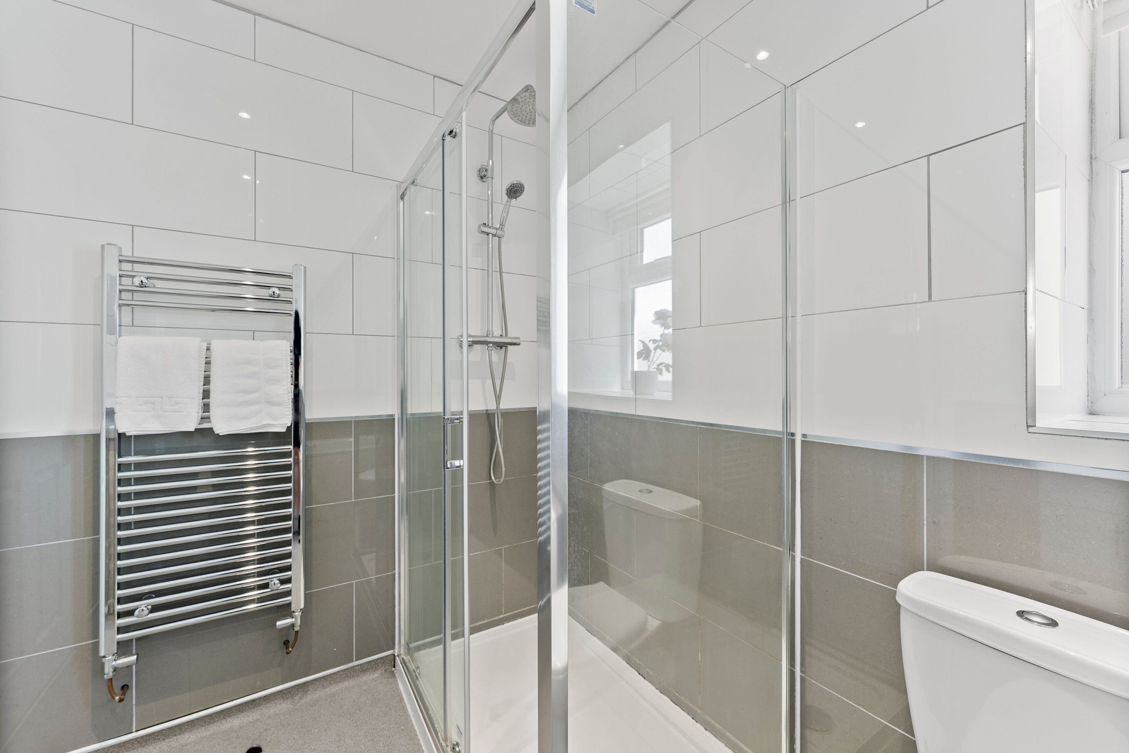 A modern bathroom with a glass-enclosed shower, a glass-enclosed toilet, and a towel rack with white towels.
