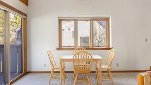 Ein Zimmer mit Esstisch und vier Stühlen, einem Fenster mit Jalousien und einem Deckenventilator.