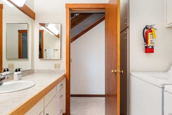 A bathroom with a wooden vanity, a sink, and a mirror. There is a fire extinguisher mounted on the wall. - Outpost: Dogwood 2724 - Aspens Location! (Wilson)