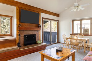 A cozy living room with a fireplace, wooden furniture, and a sliding glass door leading to an outdoor deck. - Outpost: Dogwood 2724 - Aspens Location! (Wilson)