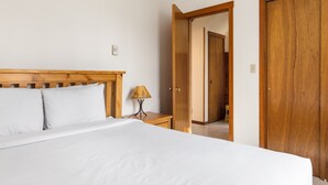 Ein Schlafzimmer mit einem hölzernen Kopfteil, einem Bett mit weißer Bettwäsche, einem Nachttisch mit einer Lampe und einem Holzschrank.