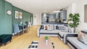 Una sala de estar moderna con sofá, mesa de comedor y sillas. Se observa una cocina al fondo, con armarios y electrodomésticos.