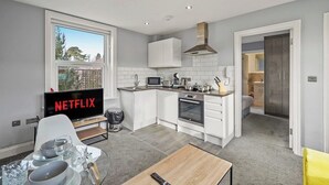 Ett modernt kök med vita skåp, en mikrovågsugn och en spis. Det finns en matplats med ett bord och stolar, och en tv-skärm som visar "NETFLIX".