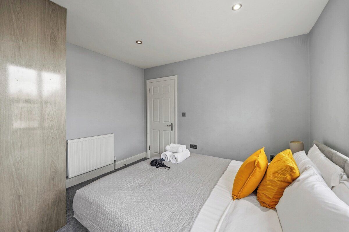 A bedroom with a bed, white bedding, two yellow pillows, a white door, and a radiator.