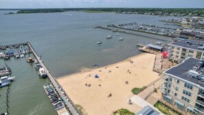 En småbåtshamn med förtöjda båtar, en sandstrand och en byggnad med en balkong som vetter mot vattnet.