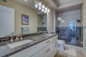 A modern bathroom with a granite countertop, two sinks, a large mirror, and a glass-enclosed shower.