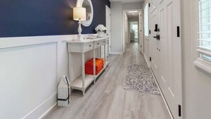 A hallway with a white console table, a mirror, and a vase with flowers. There is a patterned rug on the floor.