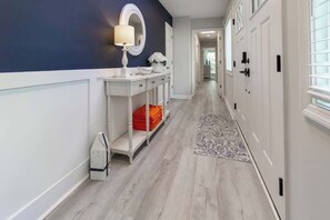 A hallway with a white console table, a mirror, and a vase with flowers. There is a patterned rug on the floor.