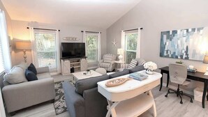A modern living room with a sofa, armchairs, a TV, and a dining table.