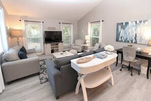 A modern living room with a sofa, armchairs, a TV, and a dining table.