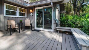 A wooden deck with a table and chairs, a bench, and a sliding glass door leading to an outdoor area.