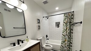 A bathroom with a white sink, mirror, toilet, and bathtub. There are ceiling lights, a shower curtain, and a small window with a star decoration. - 2 King Beds + 400ft from Beach - 8 (norfolk)