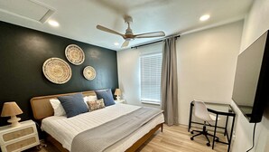 A modern bedroom with a bed, bedside table, lamp, wall decor, ceiling fan, window with blinds, and a desk with a chair. - 2 King Beds + 400ft from Beach - 8 (norfolk)