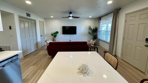 A modern living room with a white marble dining table, a red sofa, a ceiling fan, and a TV mounted on the wall. - 2 King Beds + 400ft from Beach - 8 (norfolk)