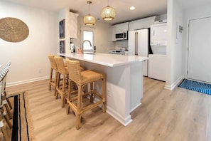 A kitchen with a central island, white cabinets, and a dining area with wicker chairs.