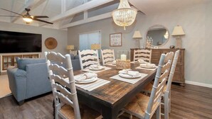 Un comedor con mesa de madera, sillas blancas y una araña.