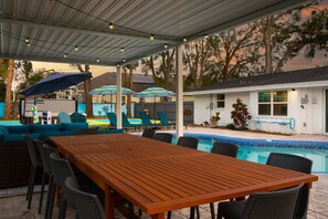 A covered outdoor area with a pool, lounge chairs, and a wooden table.