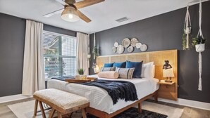 Une chambre à coucher comprenant un lit, des tables de chevet, un banc, un ventilateur de plafond et des éléments décoratifs sur les murs.