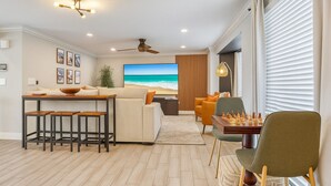 Un salon moderne avec un plancher en bois, un canapé, une table basse, un téléviseur et une table d’échecs.