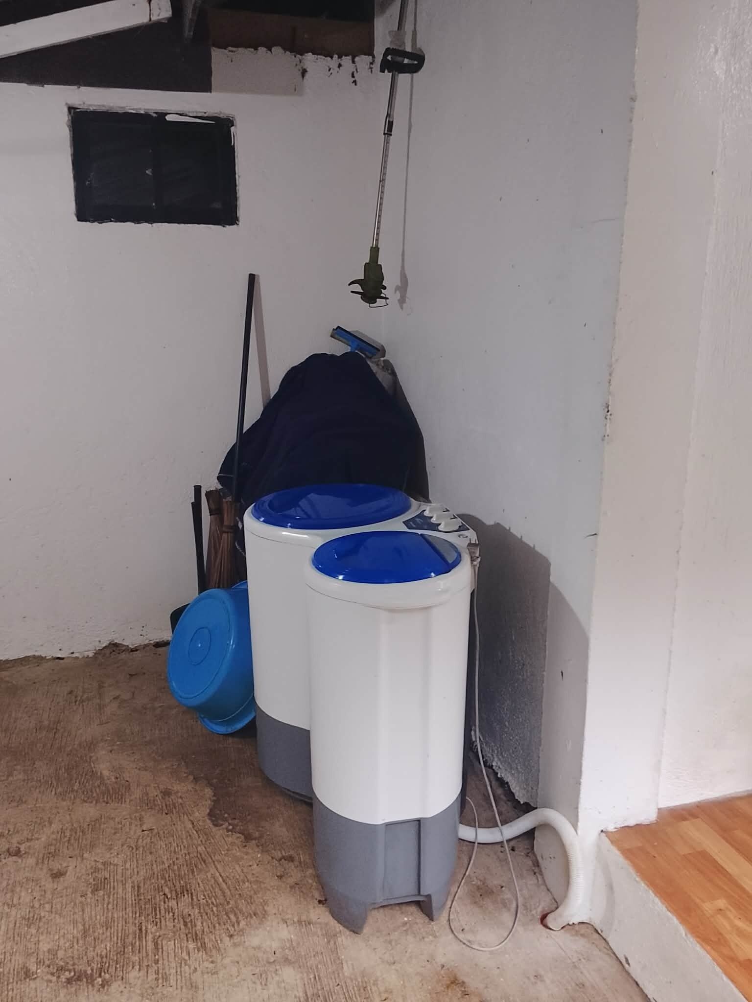 A corner of a room with two large water tanks, a hose, and a wooden floor.