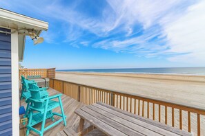 A wooden deck with chairs and a table overlooking a beach. - Oceanfront beach house just steps from the Atlantic in South Nags Head! (South Nags Head)