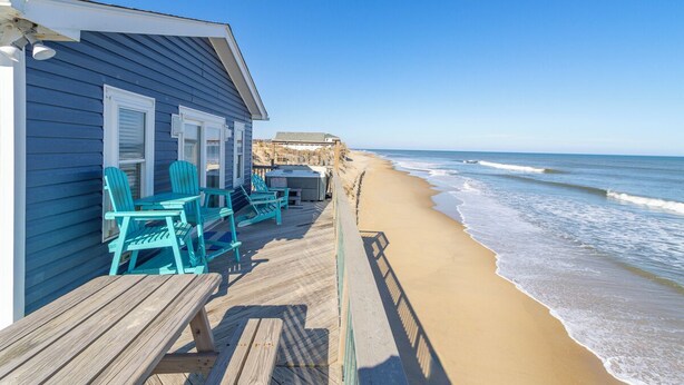Ein Strandhaus mit einer Holzterrasse, türkisfarbenen Stühlen und Blick auf den Ozean.