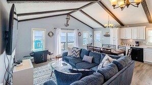 Ein geräumiges Wohnzimmer mit einer großen, blauen Couch, einem Glastisch und einem Essbereich mit Holztisch und Stühlen.