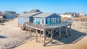 Ein Strandhaus mit einer Terrasse, einer überdachten Veranda und einem sandigen Strand im Hintergrund.
