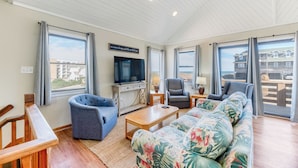 Uma sala de estar com televisão, duas poltronas, um sofá e uma mesa de centro de madeira.