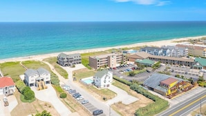 Vista aérea de uma área costeira com um hotel e vários edifícios, uma praia e um estacionamento.