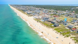 Vista aérea de uma cidade costeira com uma extensa praia de areia, edifícios residenciais e uma visão clara do oceano.