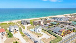 Vue aérienne d’un complexe hôtelier situé sur la côte, comprenant plusieurs bâtiments, une plage et un parking.