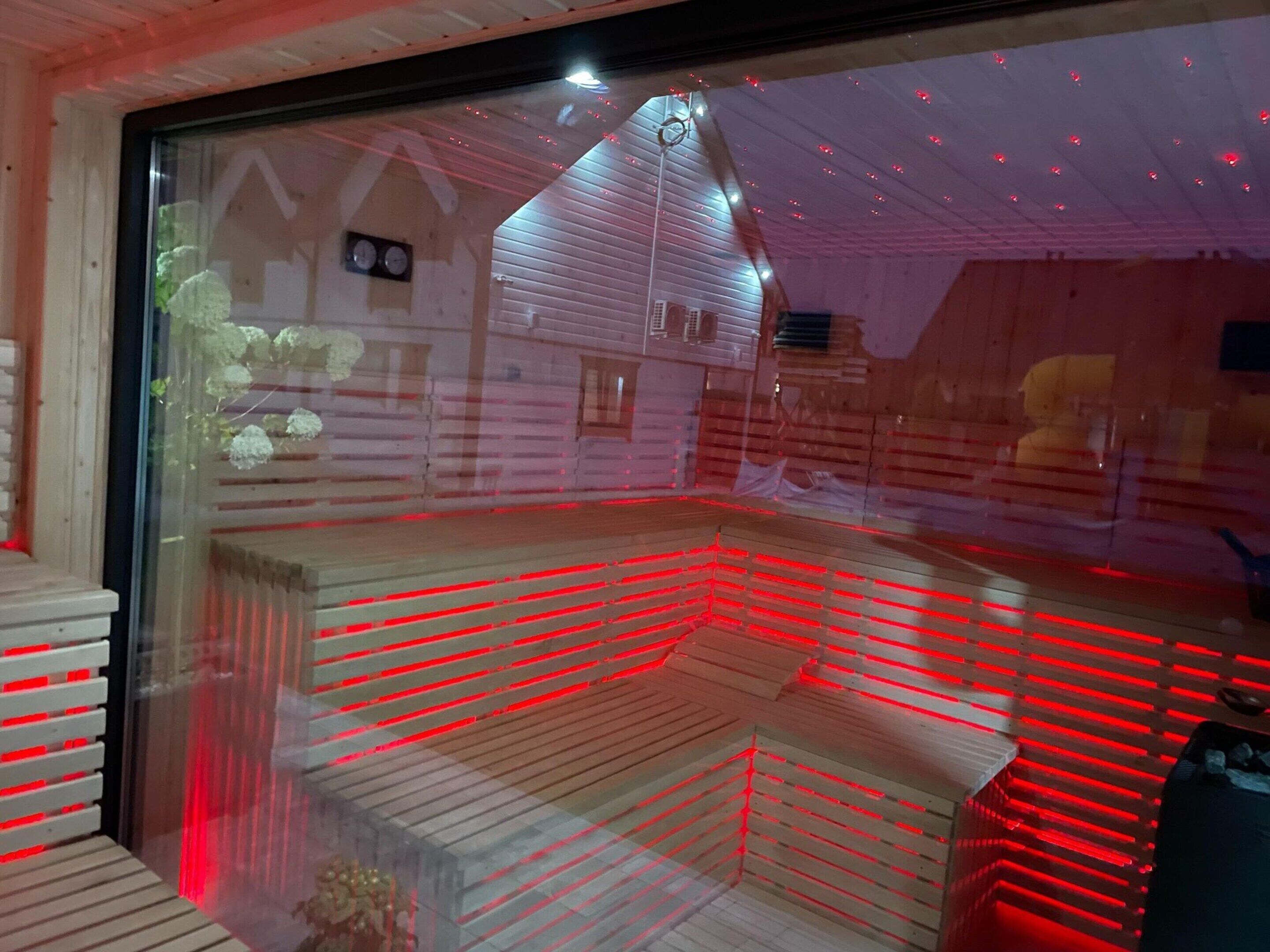 A room with a large window, wooden flooring, and a visible ceiling with red lighting.