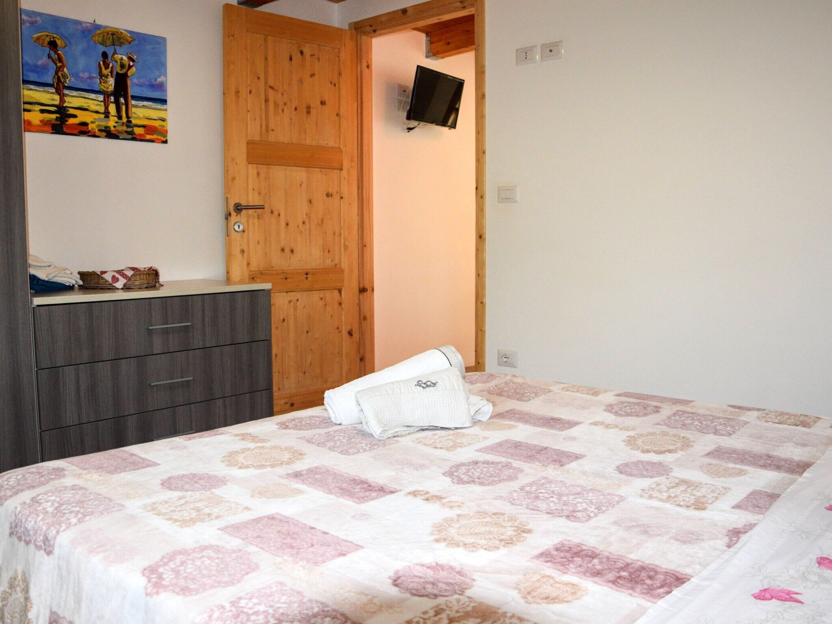 A bedroom with a bed, a wooden door, a television, and a painting on the wall.