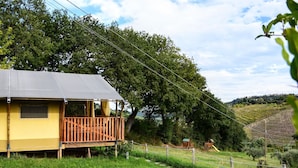 En gul stuga med en träveranda och en inglasad veranda, omgiven av frodig grönska och ett kuperat landskap.