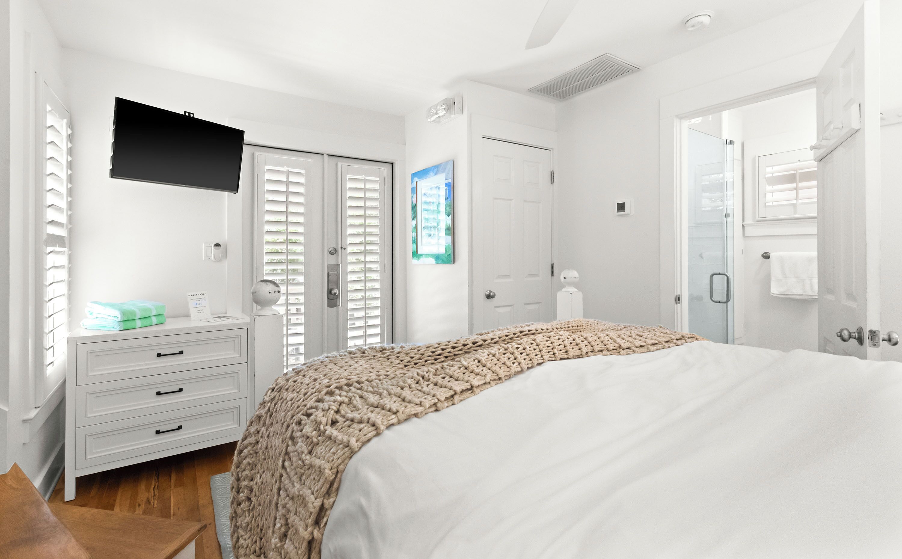 Une chambre à coucher comprenant un lit, une commode, un téléviseur fixé au mur et une porte avec une fenêtre.