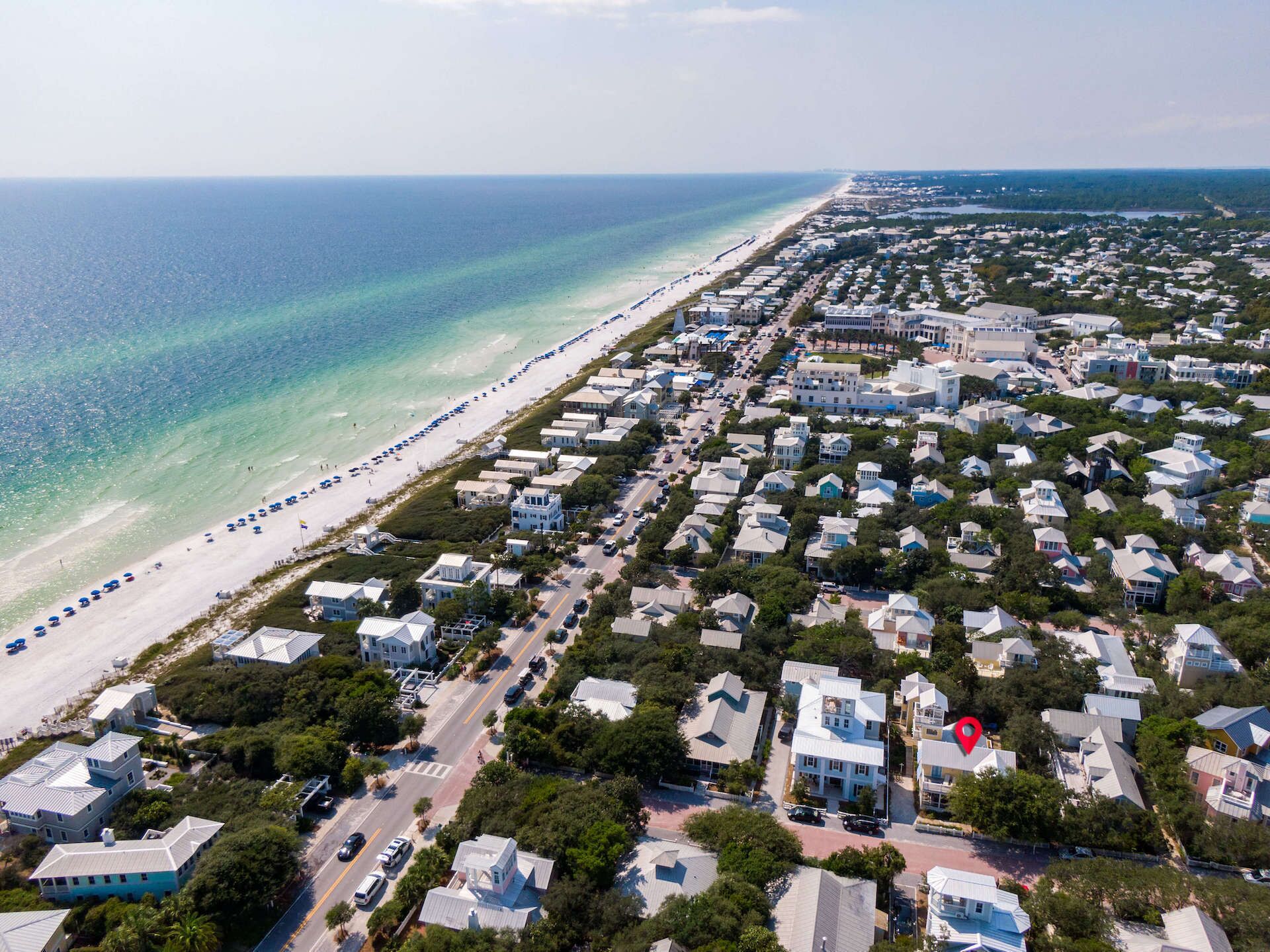 An aerial view of a coastal residential area with houses, a beach, and a road.