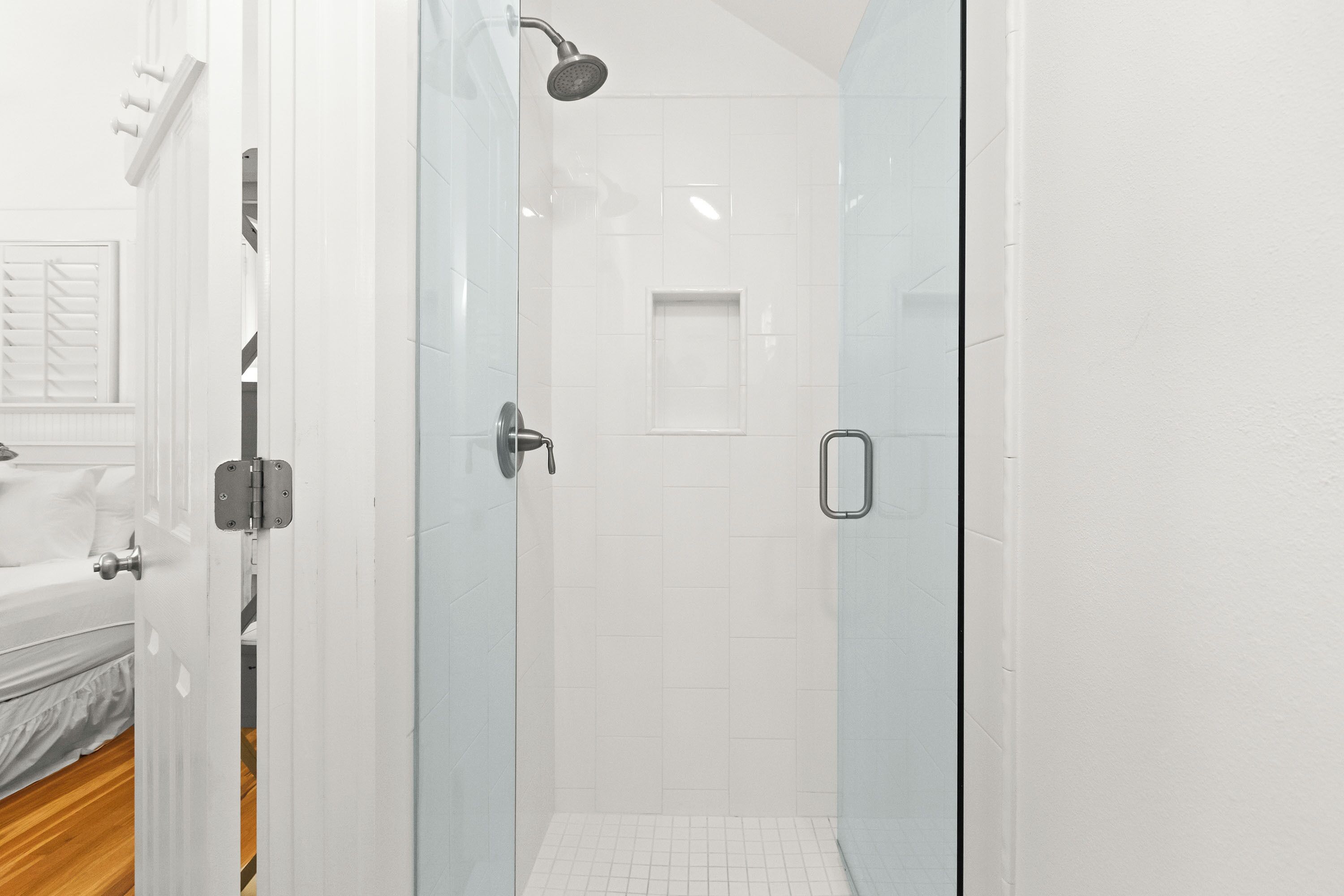A modern bathroom with a glass shower enclosure, white tiled walls, and a visible showerhead.