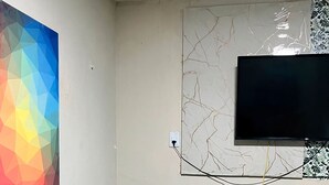 Una sala de estar moderna con un sofá gris, un cuadro abstracto lleno de color, un televisor de pantalla plana montado en la pared y una pequeña mesa blanca con una planta.