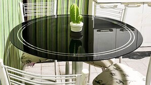 Un pequeño comedor con una mesa redonda negra, sillas blancas y una planta en maceta.