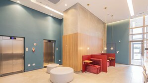 Un hall d’entrée moderne doté de deux ascenseurs, d’un mur décoratif en bois et d’un espace salon avec des meubles rouges et blancs.