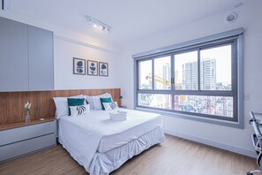 Ein modernes Hotelzimmer mit großem Fenster, einem ordentlich bezogenen Bett, einem Holz-Kopfbrett und einem kleinen Nachttisch mit Blumen.