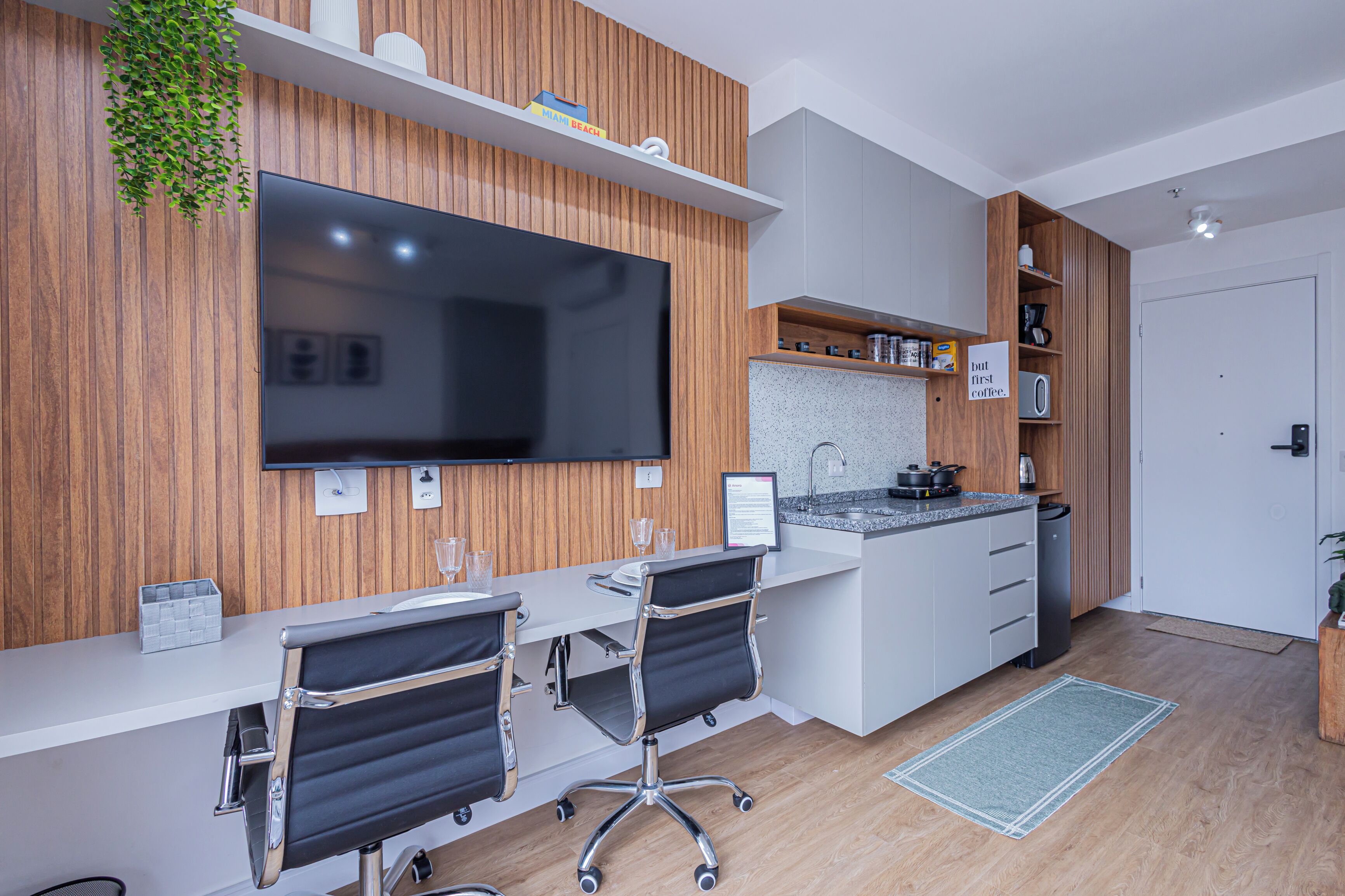 A modern kitchen with a large flat-screen TV, wooden paneling, a white countertop, and a built-in oven.