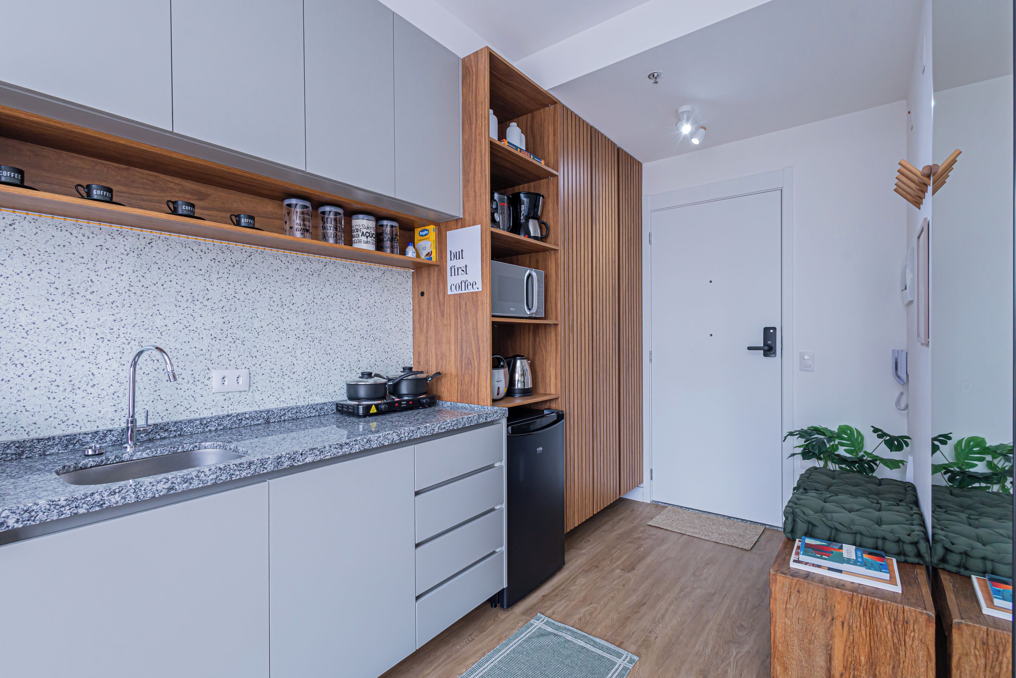A modern kitchen with a granite countertop, stainless steel sink, and wooden shelves.