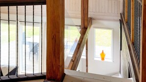 Un escalier en bois avec une rampe, une vue sur un patio extérieur avec des chaises, et une fenêtre avec un luminaire suspendu.