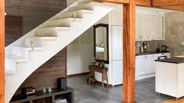 Une cuisine moderne avec des meubles blancs, un plan de travail noir et un escalier en bois.